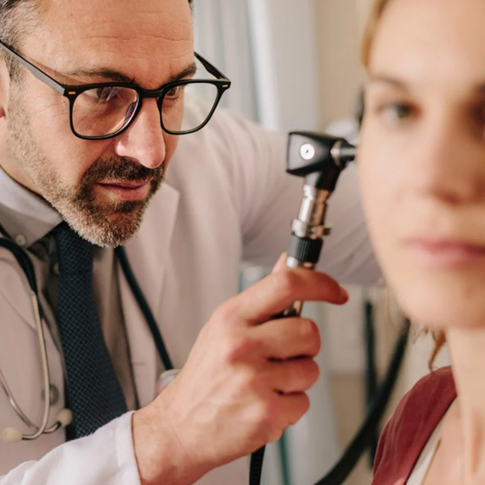 Doctor performing otoscopy on middle aged woman, possibly in preparation for earwax removal