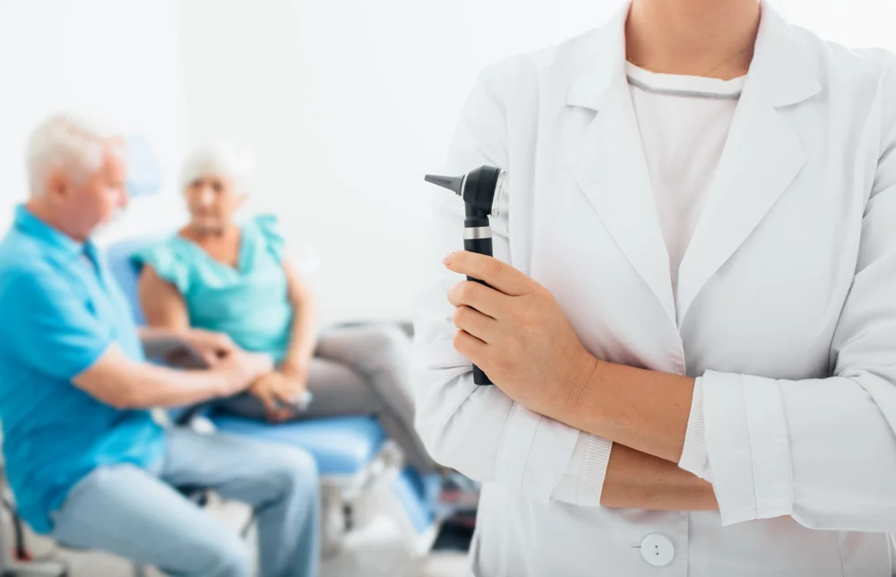 Woman hand holding otoscope with elderly couple sitting in back