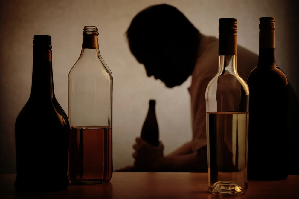 Man drinking alcohol sitting next to various bottles