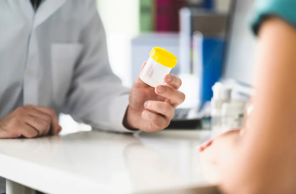 Medical professional handing a urinalysis bottle to patient for drug and alcohol testing