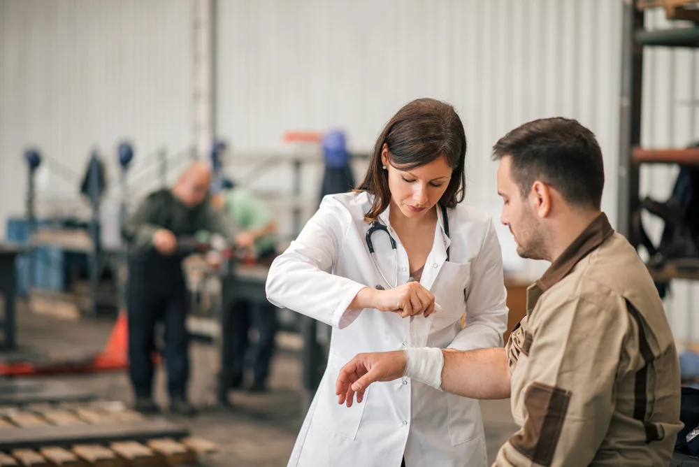 Female occupational health technician assisting injured male warehouse employee by putting a bandage around his wrist