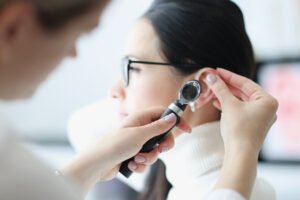 Doctor performing otoscopy on young female patient with dark hair wearing a white turtleneck shirt.