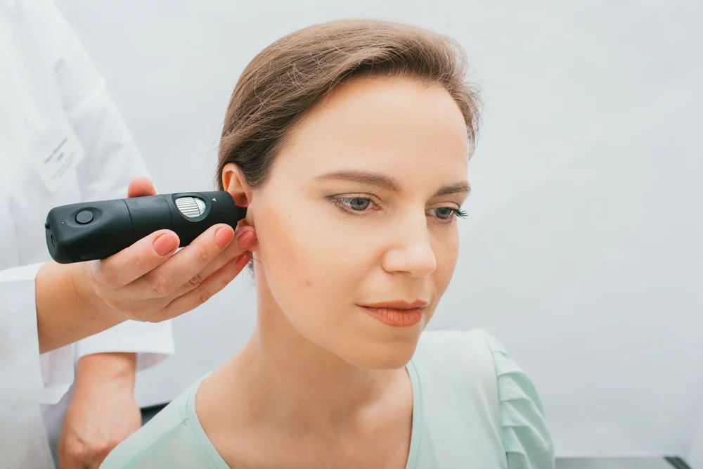 Young female with light brown hair wearing a sage green shirt having otoscopy performed on her with a video otoscope.