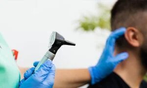 Audiologist holding an otoscope, about to examine the ear of a man.