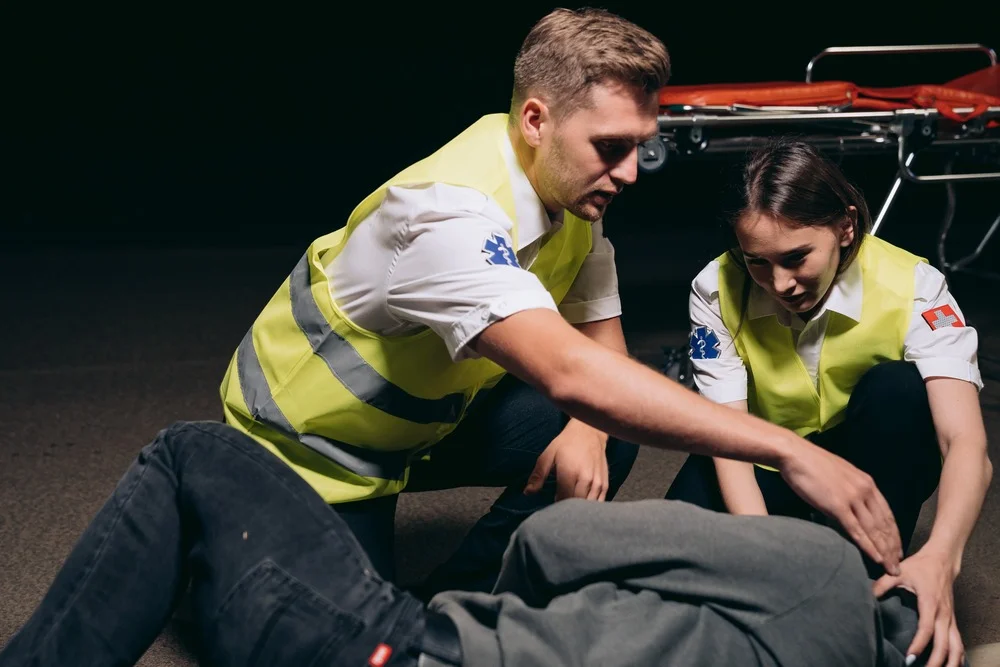 A female and a male first-aid responders helping an individual on the floor.